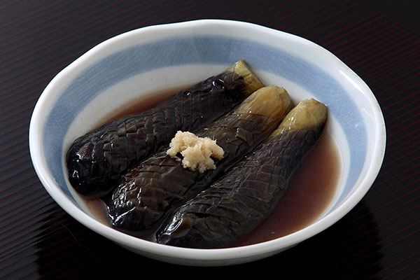 器に３切れの茄子の煮浸しを盛りつけおろしショウガを添え、濃い小豆色のお盆に乗せて撮影した画像