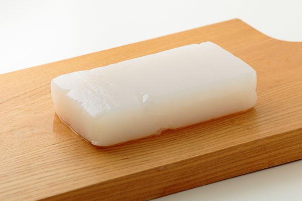木製のまな板にのせて白いこんにゃく1カット。背景は白。レシピ