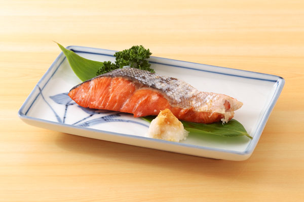 焼いた紅鮭を皿に笹の葉を敷き盛りつけ、パセリと大根おろしを添えて、明るい木目のテーブルで撮影