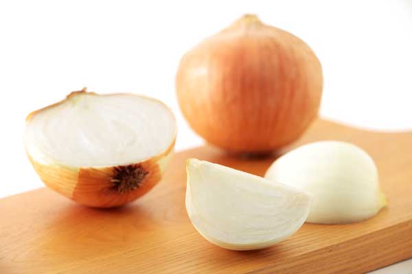 まな板の上、手前に4分の1に切ったタマネギ2片置いて、背後に1個と半分に切ったタマネギを置いた写真