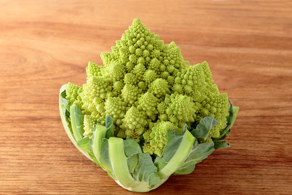 ロマネコス 野菜の画像2枚。ロマネコス一株を木目の粗い板の背景に置いて撮影。正面から1カット、斜めに置いたバリエーション1カット。