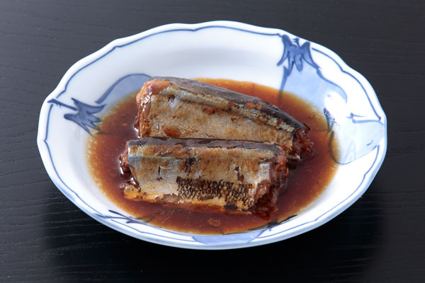 サンマの生姜煮2切れと煮汁を器に盛りつけた写真。背景は木目の黒っぽいお盆 