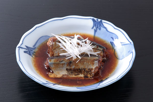 サンマの生姜煮2切れと煮汁を器に盛りつけ上に白髪ネギを添えた写真。背景は木目の黒っぽいお盆