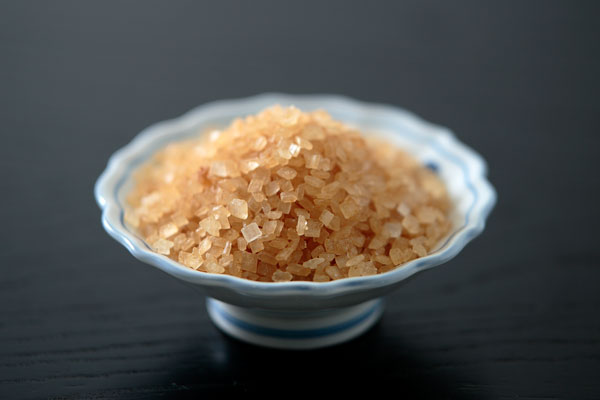 黒い木目のお盆に置いた器にザラメ糖を盛り上げ、一部分にピントを合わせたアップイメージ画像 1カット。